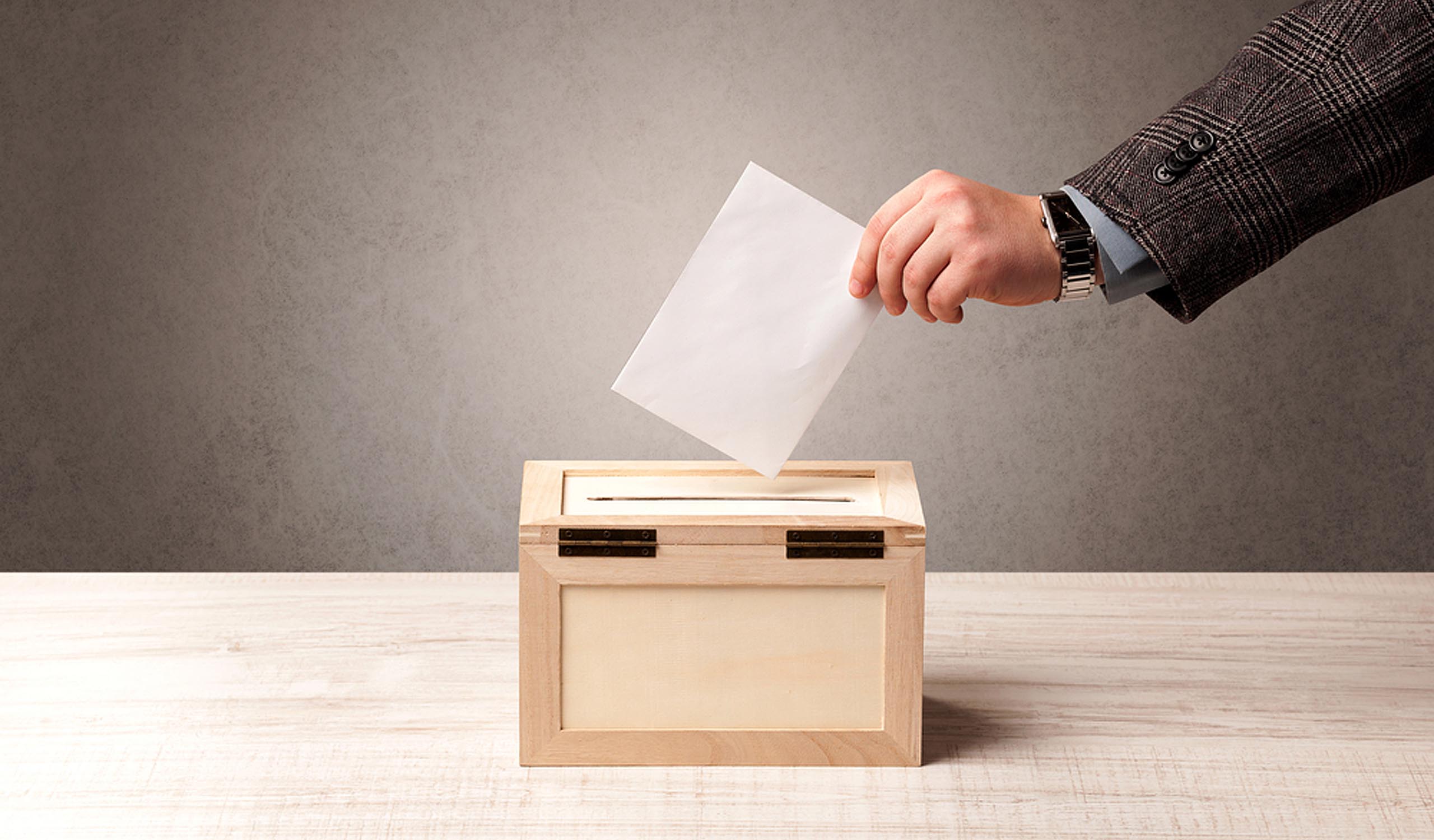 Ballot box with person casting vote on blank voting slip, brown wall background