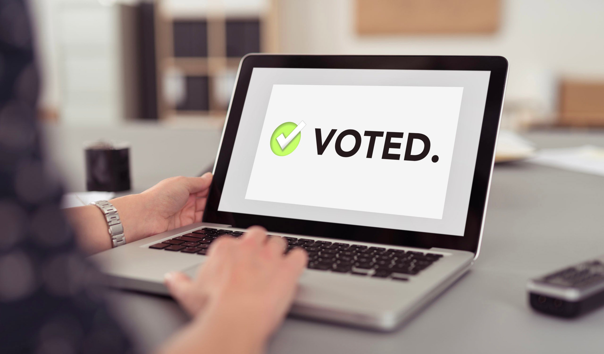 Woman on laptop with a message on the screen that has a checkmark and the text saying "voted"